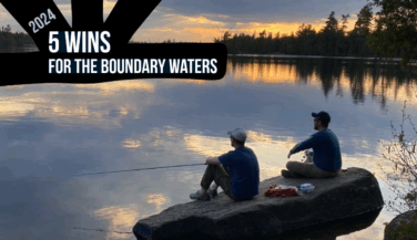 Two people sitting on a rock looking at a sunset in the Boundary Waters